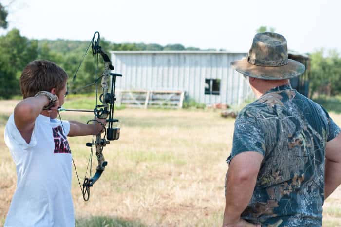 Youth aiming a compound bow at a target with his coach